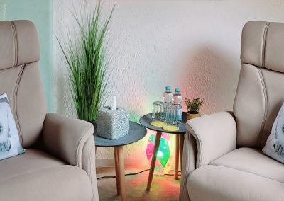 2 Sessel einander zugewandt mit Kissen, in der Mitte zwei Tische mit Wasserflaschen und eine kleine Leuchte am Boden