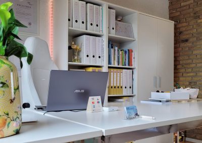 Blick auf den Schreibtisch mit geöffnetem Laptop und Regal im Hintergrund